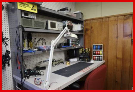 Image of the Makerspace's electronic workbench with a lamp, tools, and a mat on the desk.